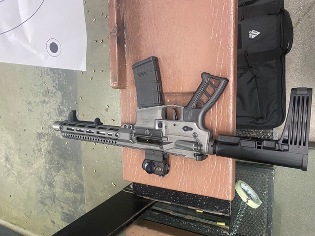 Raw aluminum AR pistol — folding brace, red dot, range bench