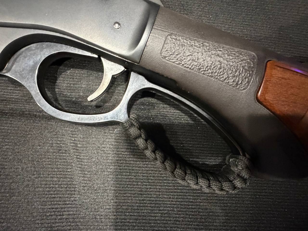 Lever-action detail — trigger group, wood forend, paracord loop